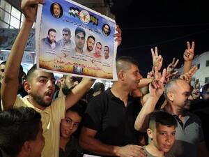 A Palestinian man flashes a poster by the militant group Islamic Jihad of 6 Palestinians who escaped from an Israeli prison, as people celebrate in the Jenin camp in the northern Israeli-occupied West Bank