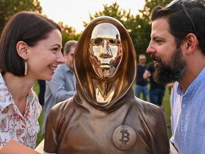 Hungarian sculptors and creators Reka Gergely (L) and Tamas Gilly (R) pose next to the statue of Satoshi Nakamoto