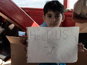 طفل يحمل لافتة استغاثة على متن سفينة للمهاجرين عالقة في المتوسط 