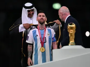 Qatar's Emir Sheikh Tamim bin Hamad al-Thani (L) wraps an abaya around Argentina's forward #10 Lionel Messi on stage next to the FIFA World Cup Trophy after Argentina won the Qatar 2022 World Cup final football match between Argentina and France at Lusail Stadium in Lusail, north of Doha on December 18, 2022. (Photo by Paul ELLIS / AFP)