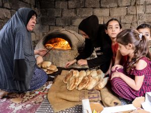 A woman bakes bread in a clay oven next to children in a home in Khan Yunis in the southern Gaza Strip. (Mohammed Abed/ AFP)