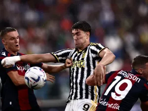 Juventus Serbian forward Dusan Vlahovic (C) fights for the ball with Bologna Swiss midfielder Michel Aebischer (L) and Bologna Scottish midfielder Lewis Ferguson during the Italian Serie A football match Juventus vs Bologna on August 27, 2023 at the “Allianz Stadium” in Turin. (Photo by MARCO BERTORELLO / AFP)