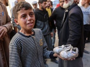 boy cries as he holds the shoes of a toddler who was killed from shrapnel following an Israeli strike