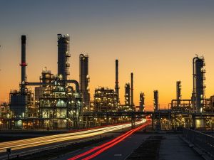 صورة خارجية لمنشأة طاقة صناعية مستقبلية عند غروب الشمس، تُظهر مصفاة نفط متقدمة بتفاصيل معقدة.