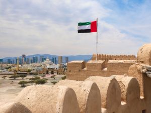 علم الإمارات العربية المتحدة يرفرف فوق قلعة الفجيرة مع أفق المدينة في الخلفية