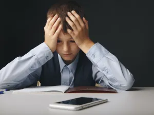 Cyberbullying concept. Stressed and upset school boy with gadget isolated.