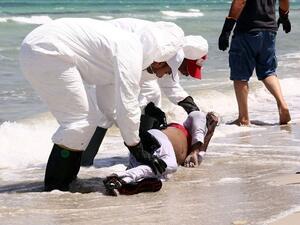 Members of the Libyan Red Crescent, wearing protective white clothing and masks, collect the body of a refugee that had washed ashore on a beach on August 28, 2015 in the port town of Zuwara. (AFP/File)