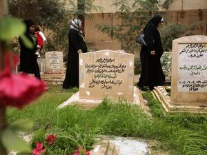 Iraqi women walk past the tomb of two unidentified Arab fighters buried in the Martyrs Cemetery of Baghdad. (AFP PHOTO/PATRICK BAZ)