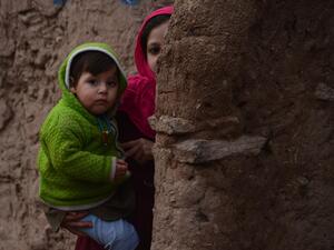 In this photograph taken on January 23, 2017, an Afghan girl holds her brother as she walks through a refugee camp in Herat. (AFP/Aref Karimi)