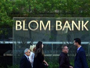 People walk past the sign of the BLOM Bank in Beirut, a day after a bomb blast hit its headquarters in Verdun. (AFP/Patrick Baz)