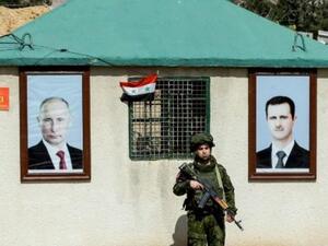 فرد من الشرطة العسكرية الروسية بين صورتي الرئيس فلاديمير بوتين وبشار الأسد عند معبر الوافدين قرب دمشق
