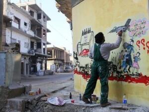 فنان سوري يرسم جدارية تمثل الحرب في بلاده، في احد شوارع بنش قرب ادلب

