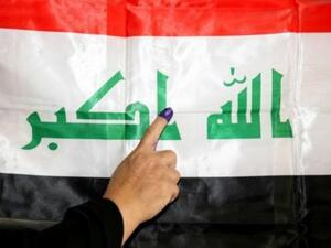 عراقية تبرز اصبعها المغطى بالحبر امام علم العراق بعد التصويت

