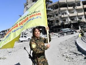 القيادية في قوات سوريا الديموقراطية روجدا فلات ترفع علم هذه القوات في دوار النعيم في الرقة

