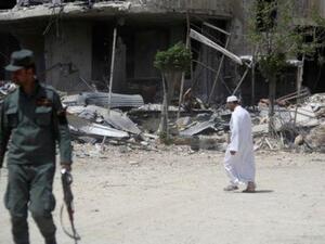 جندي من الجيش السوري يقف ممسكا بسلاحه ورجل يمر من أمام مبان مهدمة في مدينة دوما بدمشق في سوريا يوم الجمعة

