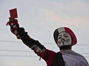 A protestor wearing a Guy Fawkes mask holds up a red card as thousands of Egyptian demonstrators gather outside the presidential palace in Cairo (Khaled Desouki / AFP)