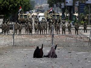 Two veiled Egyptian women, supporters of deposed president Mohamed Morsi, sit in front police standing behind barbed wire fencing that blocks the access to the headquarters of the Republican Guard in Cairo on July 8, 2013. (AFP)