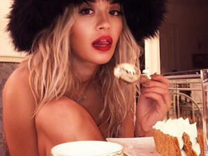 The 27-year-old singer opted for only a large oversized black fur hat as she shed the rest of her clothes to enjoy a slice of cake. (Source: @ritaora - Instagram)