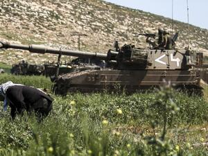 Israeli soldiers drive a 155mm self-propelled howitzer past a Palestinian farmer during a military exercise near the West Bank village of Aqraba, east of Nablus, on April 4, 2017. (AFP/Jaafar Ashtiyeh)