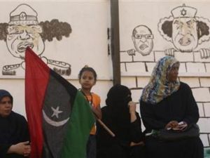 ليبيات يجلسن بالقرب من رسومات للعقيد الليبي معمر القذافي في بنغازي