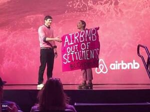A protester against Airbnb's listing of West Bank settlement rentals during an interview with Ashton Kutcher at Airbnb Open in Los Angeles in 2016. (Screenshot/YouTube)