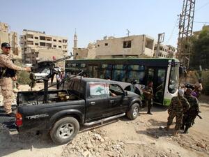 Syrian government troops stand guard as a bus carrying people drives by, as part of an evacuation from the town of Daraya outside the capital Damascus on August 26, 2016. (AFP/Youssef Karwashan)