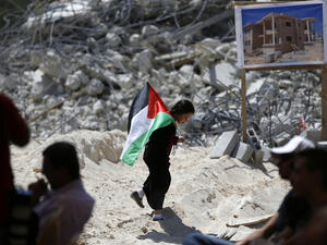 A Palestinian child holds a national flag as she walks past the rubble of Palestinian homes destroyed by Israeli authorities on July 29, 2016. (AFP/File)
