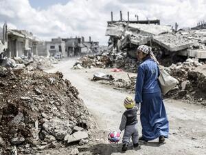 A Kurdish Syrian woman walks with her child past the ruins of the town of Kobane. (AFP/Yasin Akgul) 