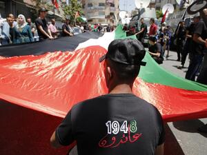 Palestinian protesters hold a large national flag as they take part in a protest marking the 69th anniversary of Nakba, near the West Bank city of Ramallah on May 15, 2017. (AFP/Abbas Momani)