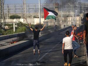 A Palestinian protester holds up a Palestinian flag in one hand while raising a crutch with another during clashes with Israeli forces near Gaza Strip on September 26, 2018.  (SAID KHATIB / AFP)