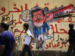 Egyptian protesters walk past graffiti against President Mohamed Morsi on the wall of the presidential palace in Cairo on July 1, 2013. (Source: AFP/GIANLUIGI GUERCIA)