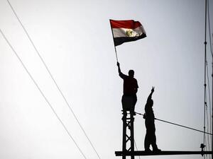 Protestor waves a flag as another makes the victory sign at the top of a Cairo electricity pole (AFP)