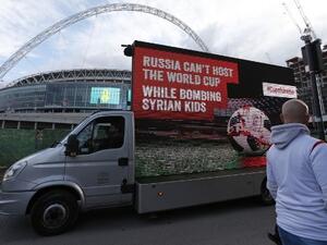 A mobile billboard showing a design of a blood-stained football on a pitch, with the words "Russia can’t host the World Cup while bombing Syrian kids", is driven past Wembley Stadium ahead of the International friendly football match between England and Italy in London on March 27, 2018.
Ian KINGTON / AFP