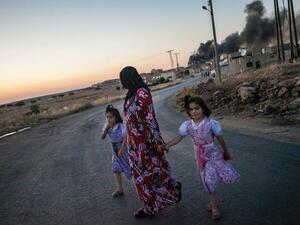 A woman walks with two children, looks back at smoke billowing in Idlib province (AFP)