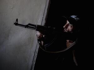 Syrian opposition fighter peers around a corner with weapon (AFP)