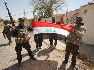Members of Iraq's mainly Shiite Popular Mobilization Units hold up an Iraqi flag.  The volunteer militia, though split into several factions, has been instrumental in the fight against Daesh militants in Iraq.  (AFP/File).  
