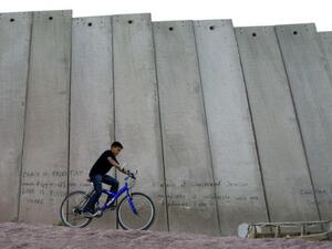 A boy rides his bike next to Israel's separation wall, which cuts off the West Bank.  Social media platform Snapchat featured the West bank July 9 after outcry following it's Tel Aviv feature on the one year anniversary of last summer's Gaza war.  (AFP/Ahmad Gharabli)