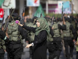 A Palestinian girl takes a photo of masked militants of Ezzedine al-Qassam Brigades, Hamas's armed wing, using her mobile phone as they parade in Jabalia refugee camp, northern Gaza Strip, on November 14, 2013, during an anti-Israel march as part of the celebrations marking the first anniversary of Israel's Operation 'Pillar of Defence'. [MOHAMMED ABED/AFP/Getty Images]
