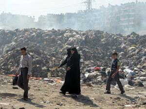 عائلة سورية تمر بالقرب من كومة نفايات ضخمة في حلب/أ.ف.ب