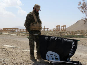 A member of the Syrian pro-government forces carries a Daesh group flag as he stands on a street in the ancient city of Palmyra on March 27, 2016. (AFP/File)