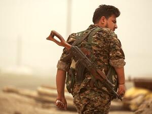 A member of the Kurdish People’s Protection Units (YPG) walks with a Kalashnikov assault rifle slung behind his back.
