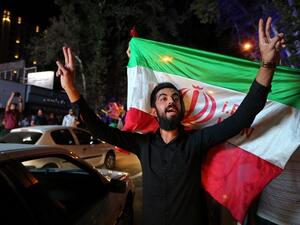 An Iranian man flashes the victory sign as another man behind him holds the Iranian flag during celebrations in northern Tehran on July 14, 2015, after Iran's nuclear negotiating team struck a deal with world powers in Vienna. (AFP/ Atta Kenare)