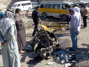 Iraqis look at the remains of a vehicle following an explosion at a small bus station . (Image credit: AFP)