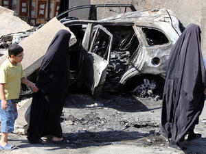 Iraqi women walk past a burnt-out vehicle on October 7, 2013 following a bombing attack in Baghdad's eastern al-Jadidah district the night before. (Image credit: AFP)