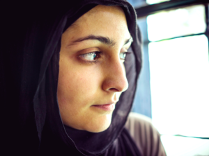 Muslim woman wearing a headscarf looks out a window. (Shutterstock)
