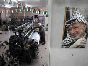 A poster of iconic keffiyeh-wearer Yasser Arafat overlooks as textile machines weave the scarves - symbols of Palestinian pride - at Hebron's Herbawi Textile Factory.  (AFP/Hazem Bader)