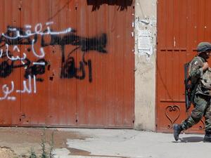  A Lebanese army soldier walks past graffiti on a closed shop which reads: "You shall fall Bashar.." in Tripoli's Sunni neighbourhood of Bab al-Tabbaneh, whose residents support the rebels battling to topple the regime in nearby Syria, during a truce with the Alawite district of Jabal Mohsen on May 27 (Joseph Eid/ AFP)