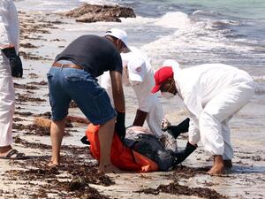 Members of the Libyan Red Crescent, wearing protective white clothing and masks, collect the body of a migrant that had washed ashore on a beach on Aug. 28, 2015 in the port town of Zuwara west of Tripoli. (AFP/Mahmud Turkia)