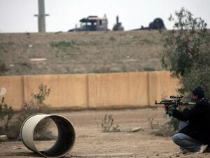 An armed Iraqi holds his rifle, as he looks towards a burnt out lorry seen at the side of the main highway leading west out of the capital Baghdad to the city of Fallujah, in Anbar province, on January 5, 2014. [AFP]