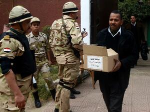 A man carries a box full of voting ballots near Egyptian soldiers standing guard outside a school that will be used as a polling station on January 13, 2014 in Cairo. [AFP]